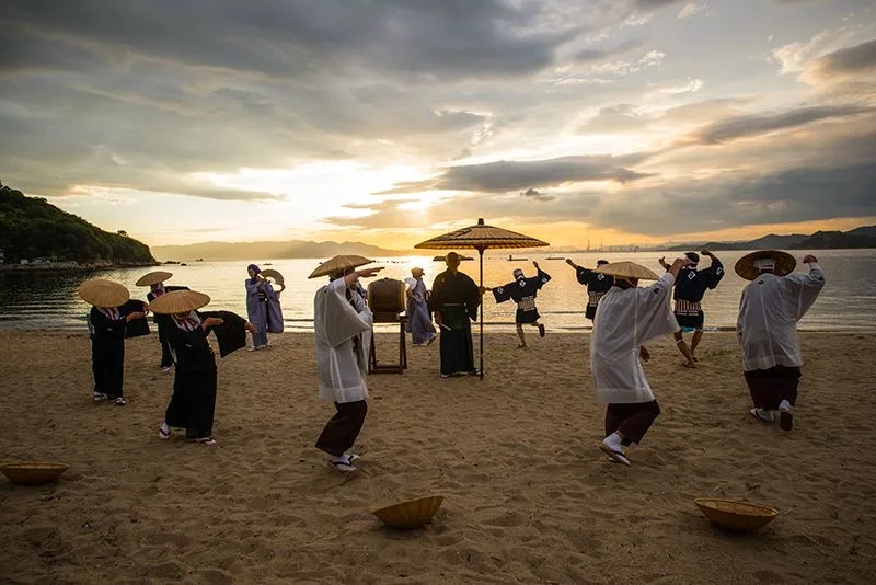 Islanders in traditional dress performing on the beach at sunset in the Kasaoka Islands