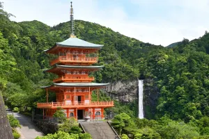 The vermilion three-storey pagoda of Seiganto-ji with Nachi Falls dropping down the cliff behind it