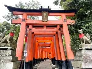The entrance torii gate and fox guardian statues at Fushimi Inari Taisha, with the tunnel of gates beyond