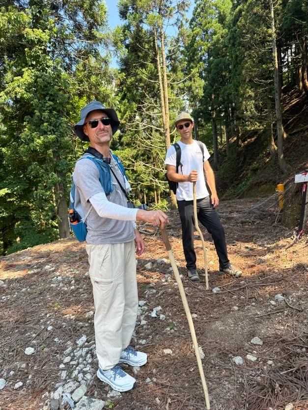 Two walkers with wooden staffs pausing on the Saba Kaido trail